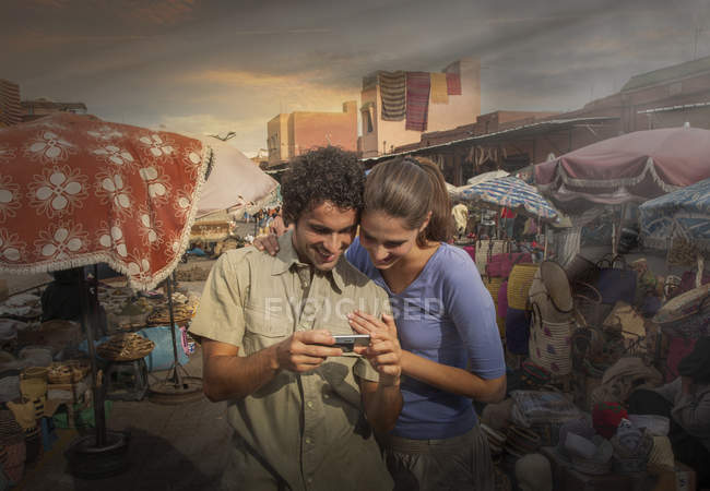 Parejas jóvenes en el mercado mirando a la cámara digital, Plaza Jemaa el-Fnaa, Marrakech, Marruecos - foto de stock