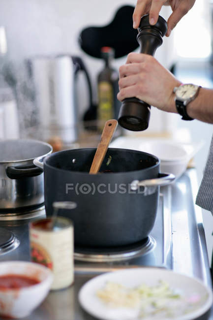 Cropped image of man grinding pepper into pot — Stock Photo