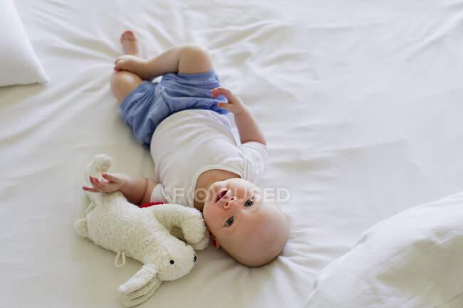 Bambina sdraiata su lenzuola con peluche — Foto stock