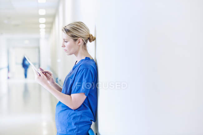 Доктор, стоящий в коридоре и рассматривающий цифровой планшет — стоковое фото