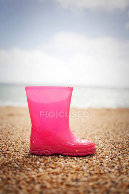 Bota de goma rosa en la playa de arena - foto de stock