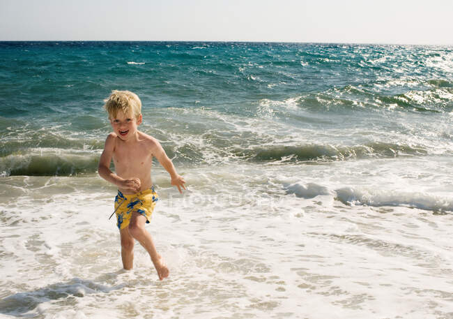 Jeune garçon à la plage en eau peu profonde — Photo de stock