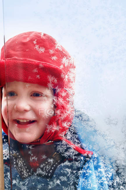 Усміхнений хлопчик дивиться у морозному вікні — стокове фото