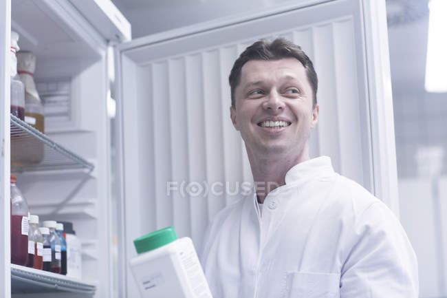Científico sosteniendo botella de producto químico retirado del gabinete - foto de stock