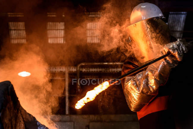 Travailleur agitant du métal fondu dans un four de fonderie — Photo de stock