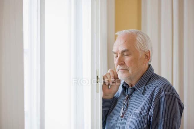 Старик, стоящий у окна — стоковое фото