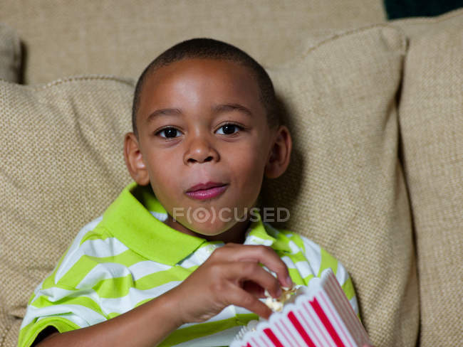 Хлопчик їсть попкорн на дивані — стокове фото