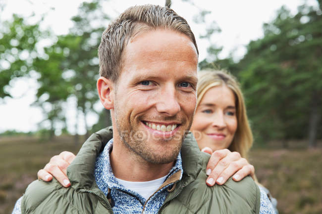 Portrait of mid adult man looking at camera, woman's hands on shoulders — Stock Photo