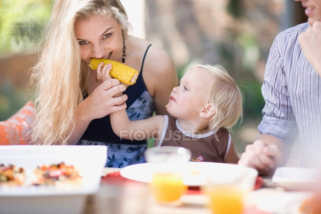 Toddler feeding mother corn outdoors — Stock Photo