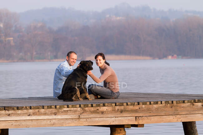 Couple petting dog on jetty over lake — Stock Photo