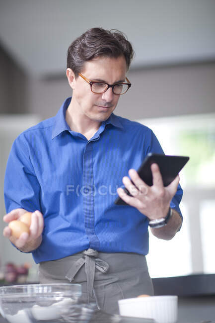 Uomo maturo che tiene le uova, guardando tablet digitale — Foto stock