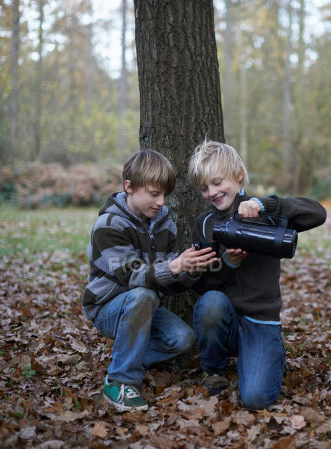Boys pouring hot drink from flask in autumnal forest — Stock Photo