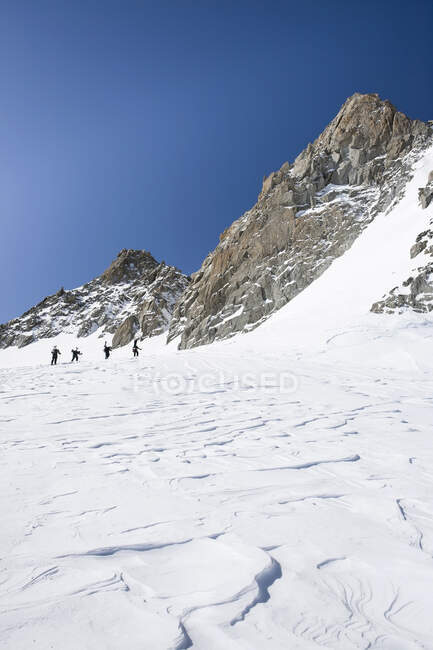 Cuatro snowboarders masculinos trepando por el paisaje cubierto de nieve, Trient, Alpes suizos, Suiza - foto de stock
