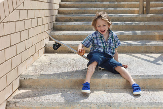 Boy sitting on skateboard on steps — Stock Photo