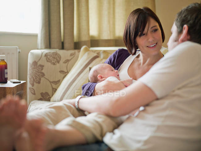 Un couple et un nouveau bébé assis sur un canapé — Photo de stock