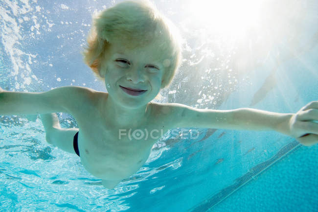 Улыбающийся мальчик плавает в бассейне — стоковое фото