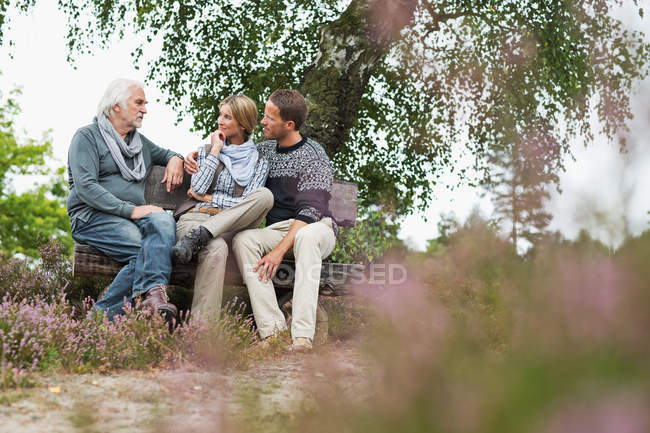 Senior man and mid adult couple sitting on log — Stock Photo