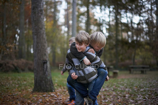 Chico dando amigo en piggyback en bosque - foto de stock