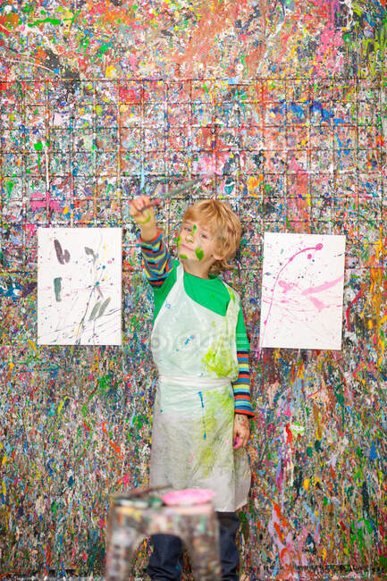 Boy in front of paint splattered wall — Stock Photo