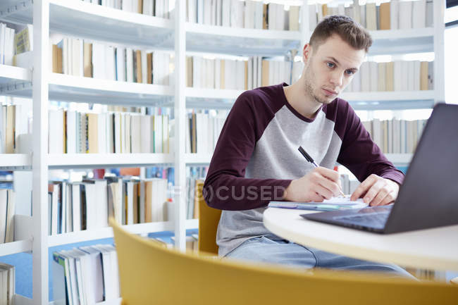 Jovem estudante universitário que trabalha na biblioteca — Fotografia de Stock
