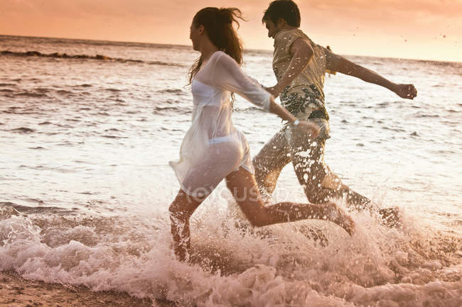 Casal correndo em ondas na praia — Fotografia de Stock
