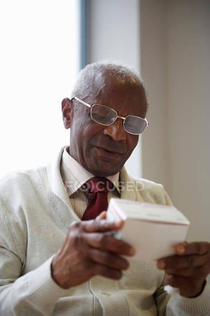 Elderly black man reading medicine box — Stock Photo