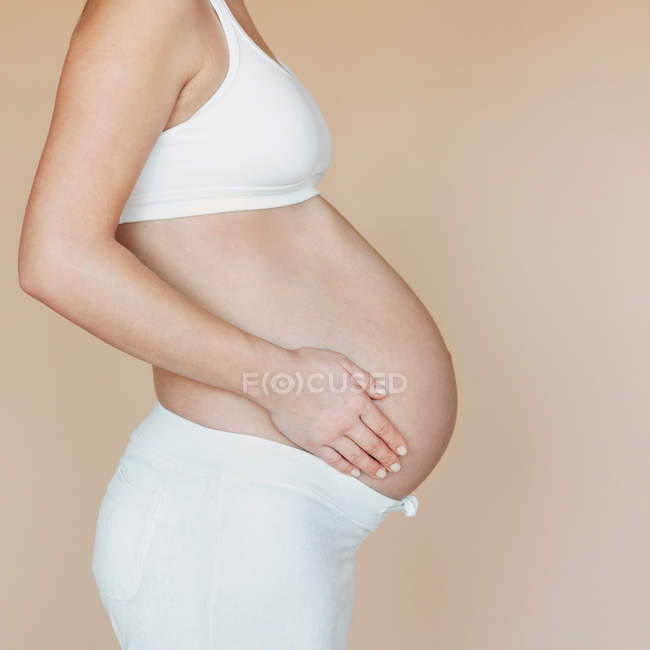 Vista cortada de um lado da mulher grávida no fundo de cor — Fotografia de Stock