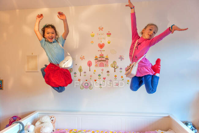 Girls jumping on bed, in mid air, arms raised — Stock Photo