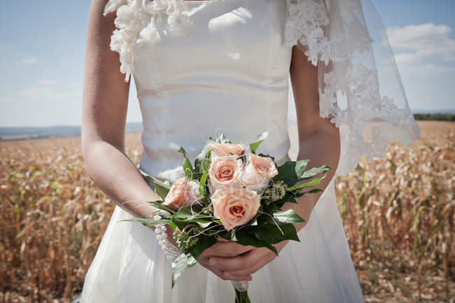 Обрезанный образ невесты в свадебном платье проведение букет в поле — стоковое фото