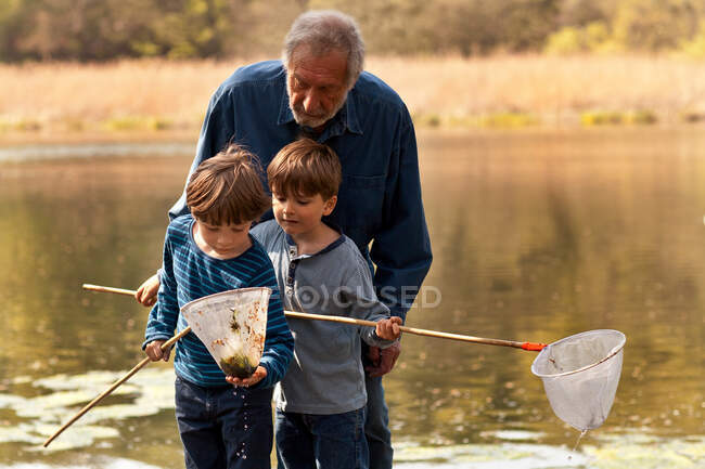 Grandfather and grandsons holding fishing nets by river — Stock Photo