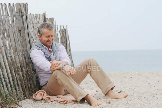 Человек сидит в песке на пляже — стоковое фото