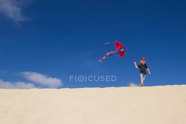 Boy flying kite on sand dune — Stock Photo