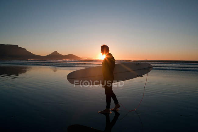 Surfista caminando en la playa al atardecer - foto de stock