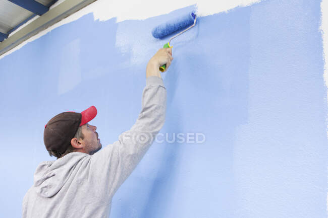 Vista trasera del hombre pintando la pared azul - foto de stock
