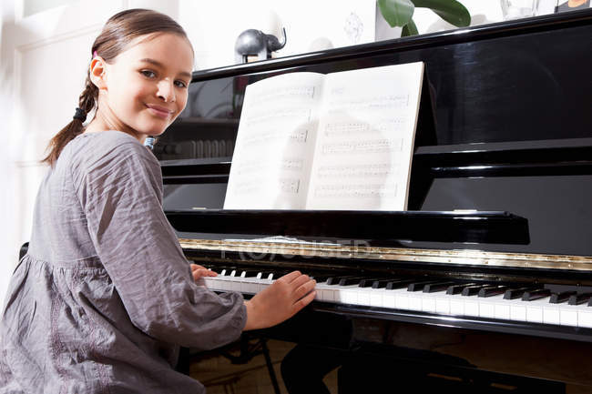 Усміхнена дівчина тренується на фортепіано, фокус на передньому плані — стокове фото