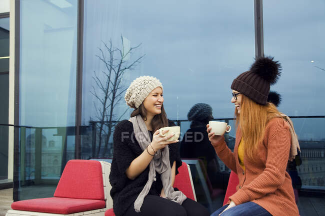 Two young adult women enjoying coffee on rooftop terrace — Stock Photo