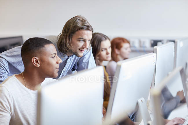 Conférencier masculin montrant un étudiant utilisant un ordinateur dans une salle informatique d'un collège d'enseignement supérieur — Photo de stock