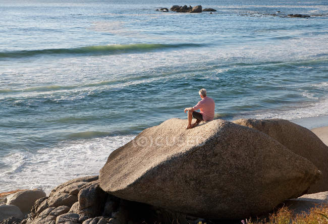 Человек сидит на валуне на пляже — стоковое фото