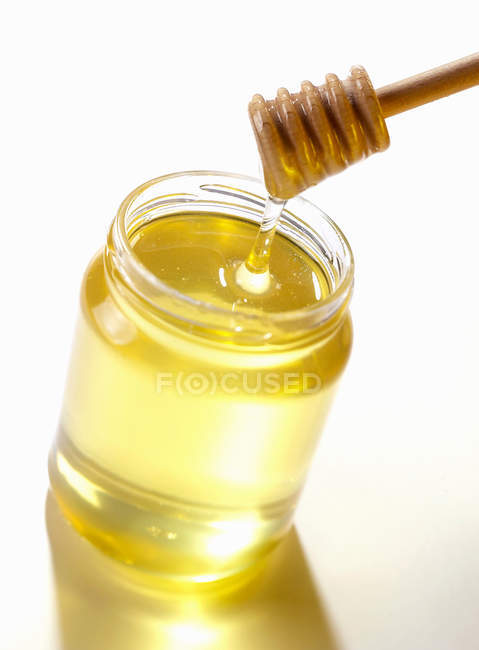 Stirrer above jar of honey on white background — Stock Photo