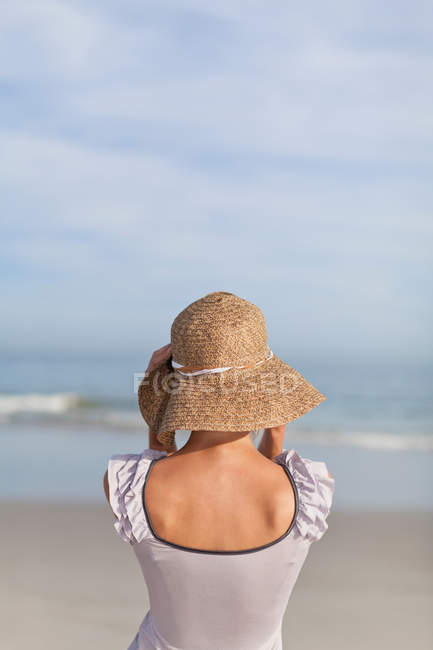 Вид ззаду жінки в солом'яному капелюсі на пляжі — стокове фото