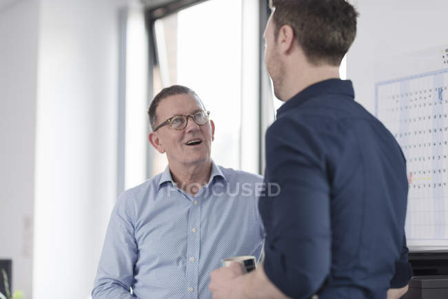 Two office workers talking while standing in office — Stock Photo