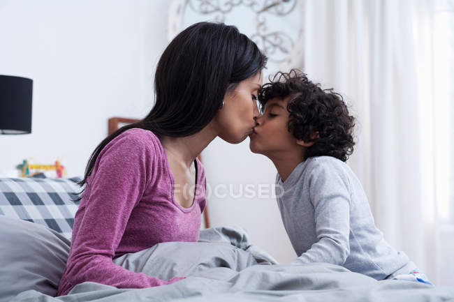 Вид збоку сина цілує мати в ліжку — стокове фото