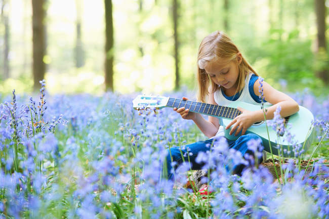 Mädchen mit Gitarre im Blumenfeld — Stockfoto