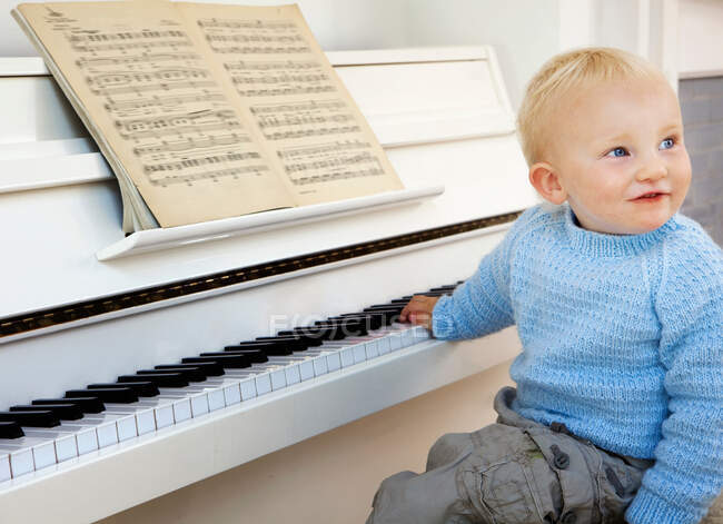 Un niño pequeño sentado al piano - foto de stock