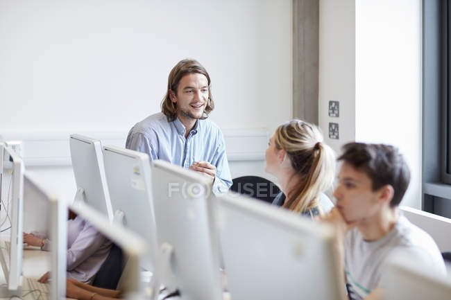 Преподаватель мужского пола беседует со студентом в компьютерном классе ВУЗа — стоковое фото