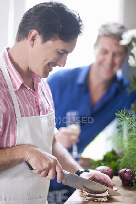 Mature man chopping red onion, man in background — Stock Photo