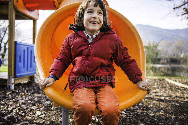 Хлопчик сидить на помаранчевому дитячому майданчику слайд — стокове фото