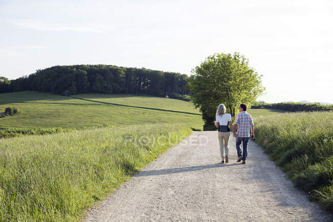 Rückansicht eines älteren Ehepaares, das auf einem Feldweg spaziert — Stockfoto
