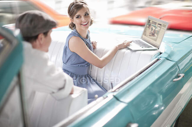 Homem assistindo mulher usar laptop no banco de trás do conversível — Fotografia de Stock