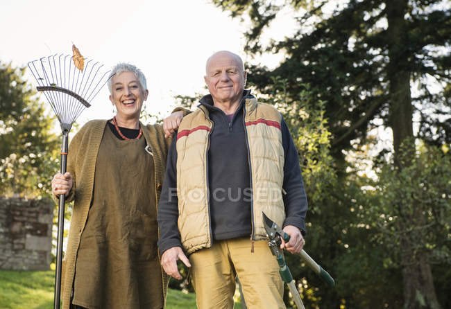 Couple aîné tenant râteau et élageur — Photo de stock